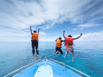 Three swimmers with life jackets hopping off of a boat